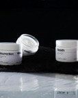 Three skincare jars labeled 'Resurrection' and 'Rebirth' on a black surface with a dark background.