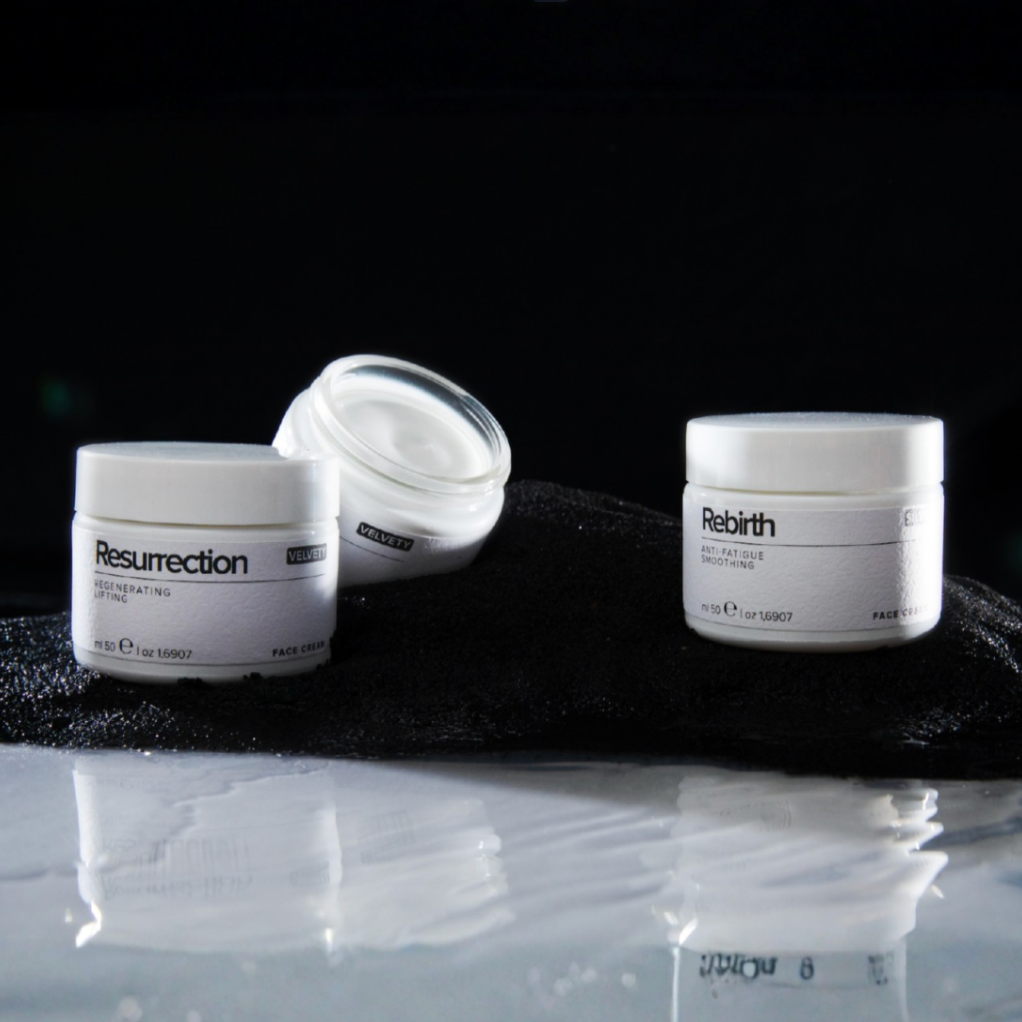Three skincare jars labeled 'Resurrection' and 'Rebirth' on a black surface with a dark background.