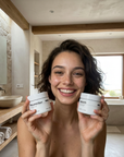Woman holding two jars of skincare  Rebirth and Resurrection in a bathroom